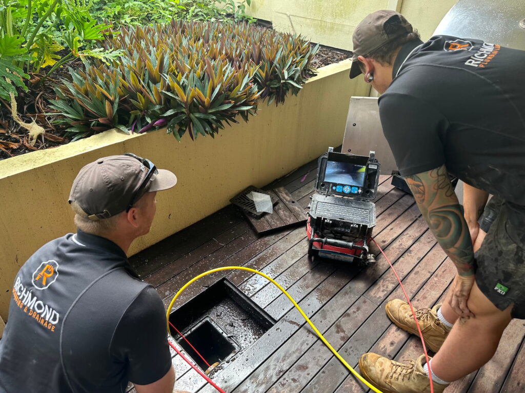 Two licensed plumbers using a modern CCTV drain camera inspection monitor to locate and clear a blocked drain in Logan.